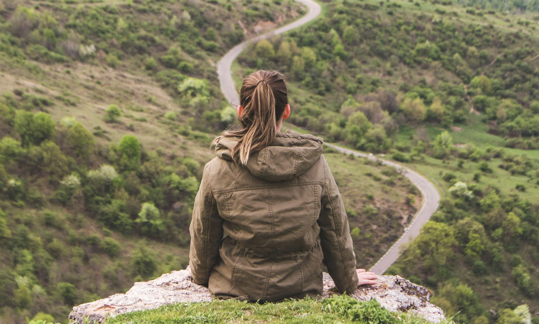 Woman sitting on top of a hill, enjoying the view.